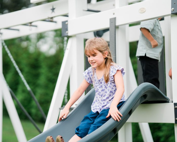 Child sliding down a playground slide with greenery in the background